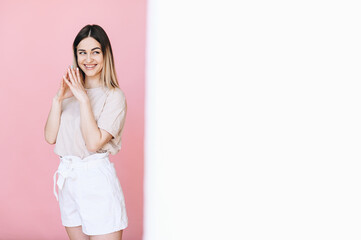 A girl stands and playfully looks to the side on a pink background, half a white background