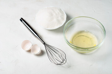 Fototapeta na wymiar ingredients for the French meringue dessert - egg white, sugar, whisk and eggshell on a gray surface