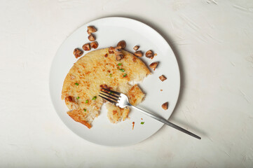 a traditional Swiss dish is potato tortilla. on a white plate is a piece of potato tortilla, fried mushrooms and a fork. leftovers on plates after meals, top view.