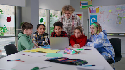 Group of multiethnic teenagers work on project together using computer in classroom