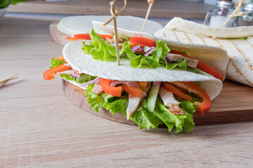 two tortillas of stuffed with fresh vegetables and chicken fillets on a cutting board and a wooden table. food trend. Fashionable way of wrapping.