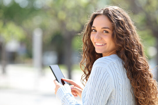 Happy woman using smart phone looking at you outside