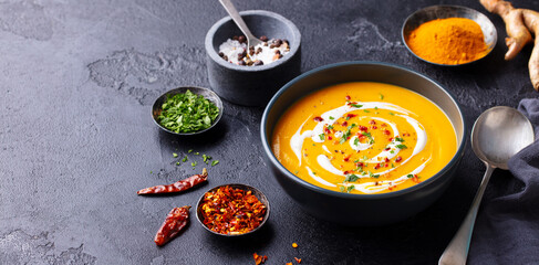 Pumpkin soup with spices in black bowl. Dark background. Close up. Copy space.