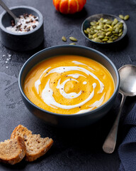 Pumpkin cream soup in black bowl. Dark background. Close up.