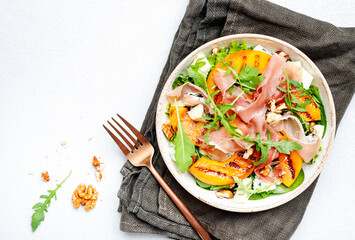 Summer salad bowl with sweet grilled peach, jamon, soft cheese, walnuts and fresh arugula on white...