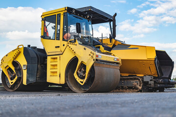 Asphalt paving machine and heavy vibratory roller close-up. A paver finisher, asphalt finisher or paving machine placing a layer of asphalt. Repaving the road surface. Road works.