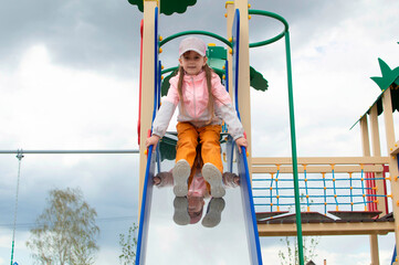 cheerful girl is rolling down a slide, a child is walking on a playground in a summer park, outdoors. happy childhood.