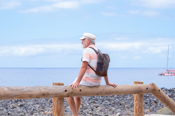 Portrait of relaxed caucasian bearded man with hat sitting at the beach looking at the horizon while enjoying vacation or retirement. Horizon over the water, copy space