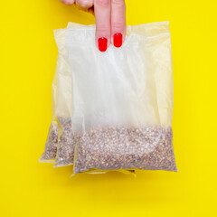 Buckwheat in bags for cooking. women's fingers with red manicure hold buckwheat. yellow background. Square image