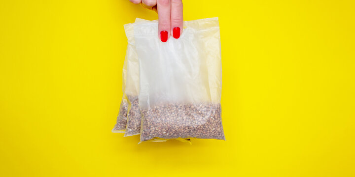 Buckwheat in bags for cooking. women's fingers with red manicure hold buckwheat. Banner for insertion into site. Place for text cope space. yellow background. horizontal image
