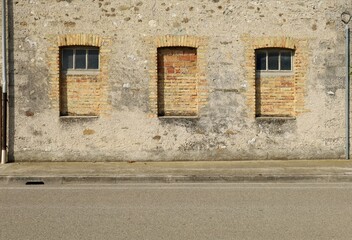 Grunge concrete wall and windows walled with bricks. Cement sidewalk and asphalt road in front. Background for copy space.