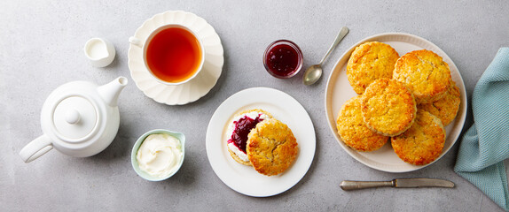 Scones, tea cakes with jam, clotted cream with tea. Traditional British teatime. Grey background. Top view. - 506370594