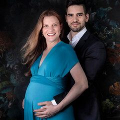 Beautiful young pregnant woman with a handsome young man wearing a suit with flowers in the background. The happy couple, married, young couple. Scotish and Spanish