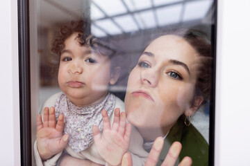Mother and daughter looking through window pressing faces on glass pane