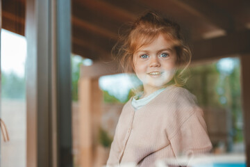 Smiling cute girl at home seen through window glass