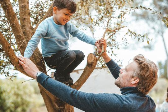 Father holding hands of son crouching on tree