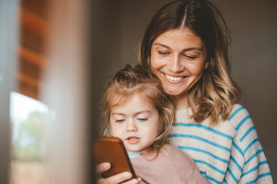 Smiling young woman showing mobile phone to daughter seen through window