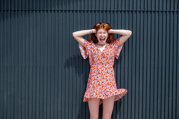 Young woman with head in hands screaming in front of corrugated iron wall