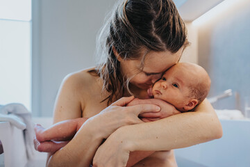 Naked mother cuddling cute baby in bathtub at home