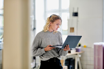 Young woman standing in office using laptop