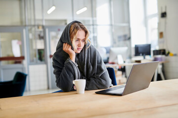 Young woman in cozy loungewear sitting at desk in office with laptop