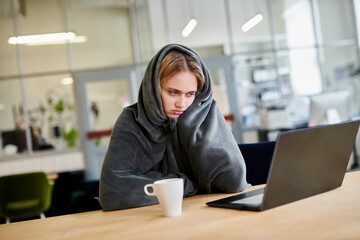 Frustrated young woman in cozy loungewear sitting at desk in office with laptop