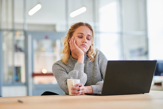 Tired young woman sitting at desk in office with laptop