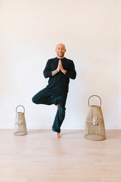 Man practicing tree pose in front of wall at yoga studio