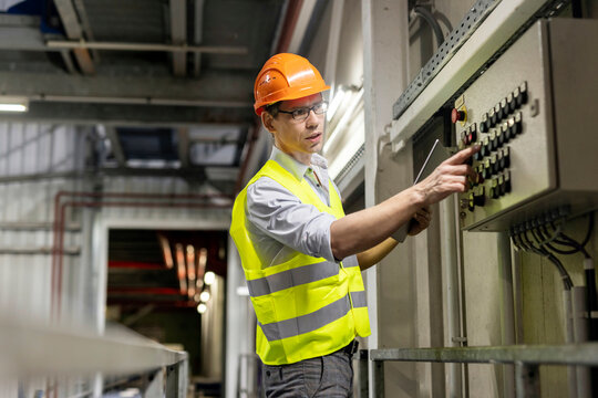 Worker with tablet PC pressing push button of control panel in industry