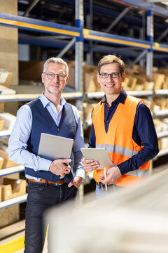 Smiling Manager And Worker With Tablet PC Standing In Warehouse