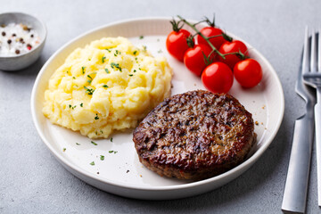 Beefsteak with mashed potato on a plate. Grey background. Close up.