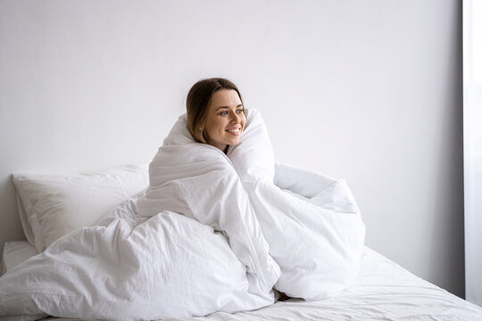 Happy woman wrapped in blanket sitting on bed at home