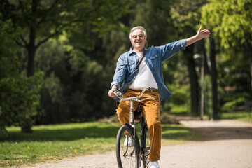 Happy senior man with arms raised enjoying bicycle ride at park