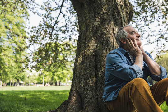 Thoughtful senior man sitting in front of tree at park