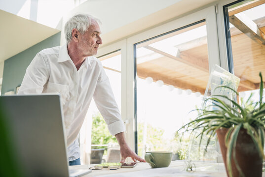 Senior Freelancer With Gray Hair Leaning On Table At Home