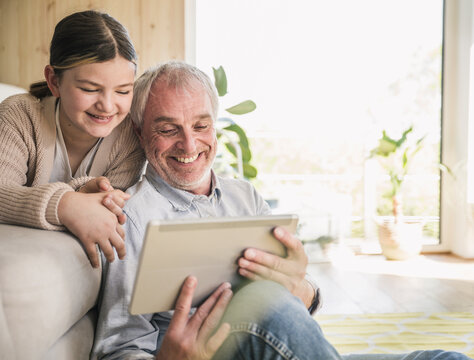 Smiling senior man with granddaughter using tablet PC at home