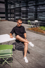 Portrait of men, in black shorts and black t-shirt, sunglasses on the street. Summer male portrait