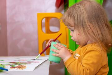 Baby girl drawing with colorful paints at home. Children development concept.