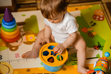 Cute little baby boy playing with colorful educational toys on the play mat in the home interior. Educational toys for little children. Early childhood development. Home activity for children