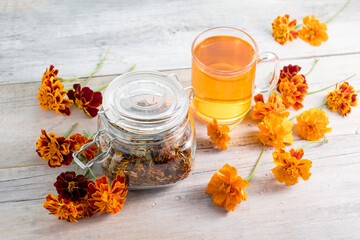 Marigold herbal tea in a glass cup, fresh and dried flowers on a white wooden table.Folk medicine.