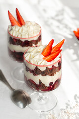 Chocolate brownie trifle with cream cheese and strawberries. Dessert in a wine glass. White table surface.