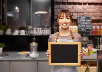 Fototapeta na wymiar service and people concept - happy smiling female barista or waitress in apron with chalkboard over bar counter at restaurant background