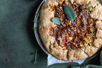 Savory tomato tart, open pie or galette with tomatoes and cheese decorated with aromatic herbs on green background. Top view.