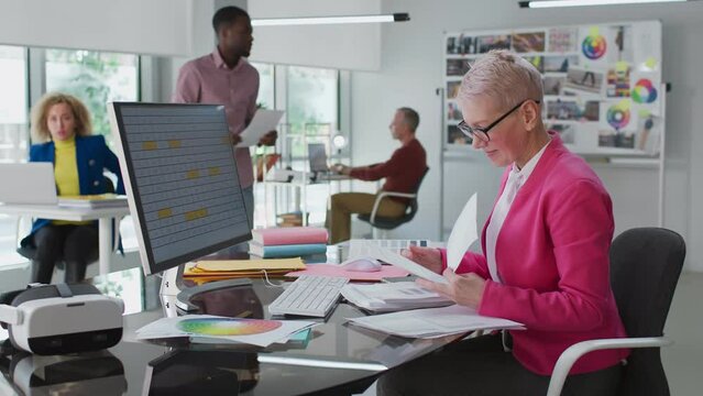 Senior woman read documents sitting at desk in modern creative office