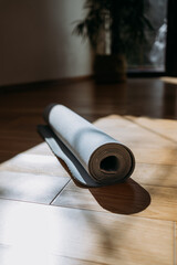 Rolled up yoga or pilates mat for exercise on natural wooden floor, sport class before or after practicing yoga, preparing for exercise, closeup