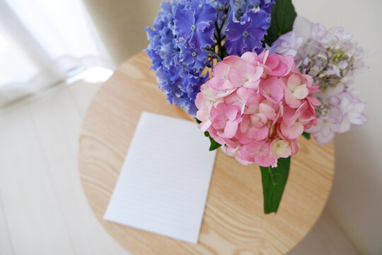 A blank letter paper with colorful Hydrangea flowers and vase on a wooden table. wedding, bridal and Birthday celebration image background. Seasonal flower interior decoration.