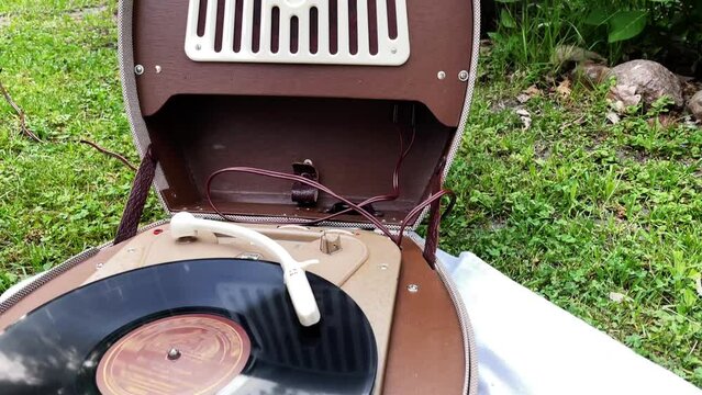 Old retro record player collectible from 1950s and 1960s is used outside in the garden to play music from a vintage vinyl record