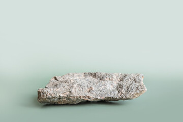 Natural gray stone stand for presentation and exhibitions on pastel green background. Abstract podium for organic cosmetic products. Minimal style.