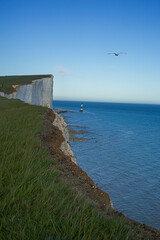 View of the red lighthouse in the bright blue water of the ocean. View of the lighthouse from the top of the cliff. Red lighthouse at the foot of the cliff.