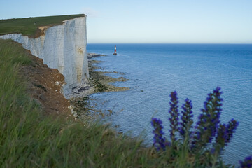 View of the red lighthouse in the bright blue water of the ocean. View of the lighthouse from the top of the cliff. Red lighthouse at the foot of the cliff.